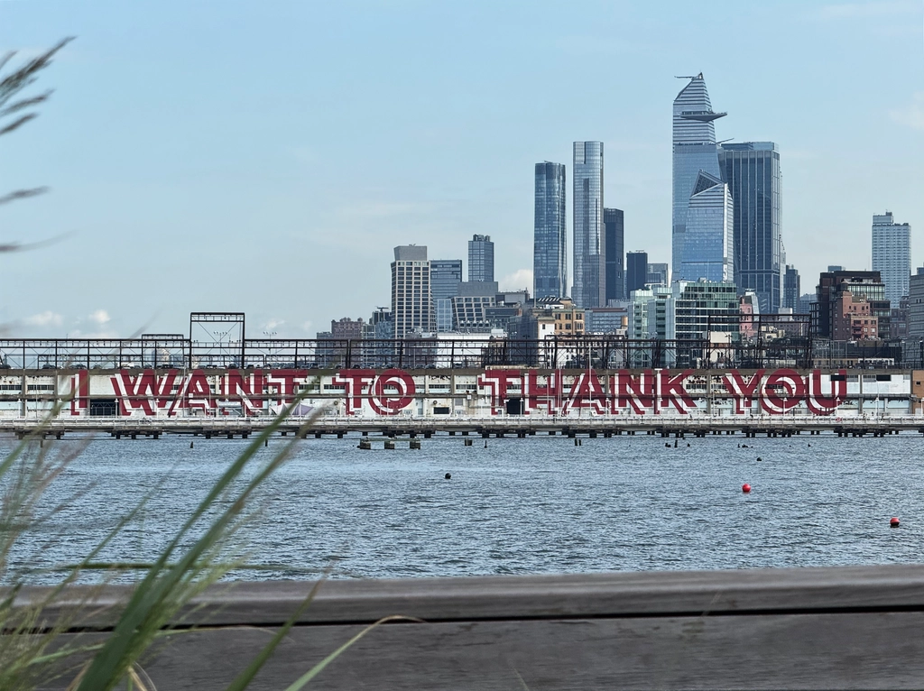 On the side of a long pier building, in front of the part of the NYC skyline that includes The Edge, is painted the words in red capital sans-serif embossed letters: I Want To Thank You