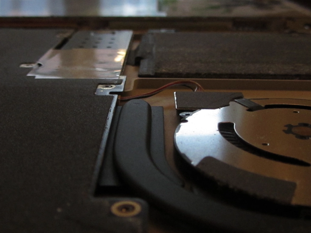 A laptop fan and battery are connected to a completely dust-protected motherboard, as viewed from a very shallow angle.